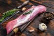 Raw fresh pork tenderloin meat on a cuuting board with cleaver. Dark wooden background. Top view
