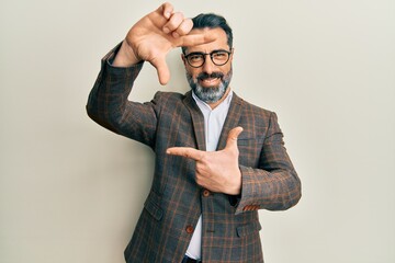 Middle age man with beard and grey hair wearing business jacket and glasses smiling making frame with hands and fingers with happy face. creativity and photography concept.