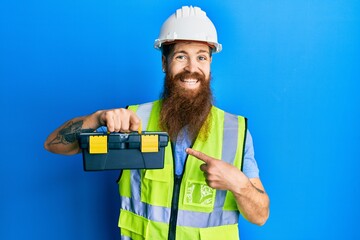 Poster - Redhead man with long beard wearing safety helmet and reflective jacket holding toolbox smiling happy pointing with hand and finger