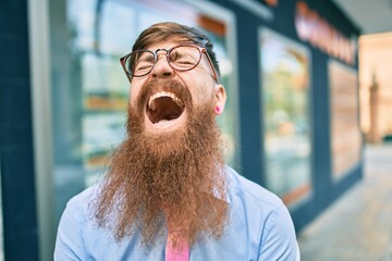 Wall Mural - Young redhead businessman with long beard smiling happy walking at the city.