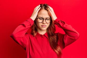 Poster - Young beautiful redhead woman wearing casual clothes and glasses over red background suffering from headache desperate and stressed because pain and migraine. hands on head.