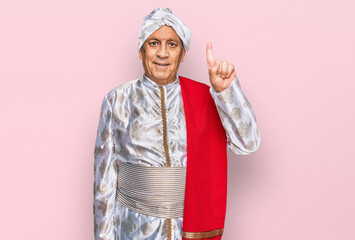 Canvas Print - Senior hispanic man wearing tradition sherwani saree clothes showing and pointing up with finger number one while smiling confident and happy.