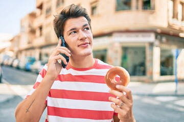 Young caucasian man talking on the smartphone eating donut at the city.