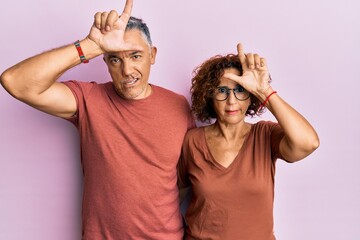 Poster - Beautiful middle age couple together wearing casual clothes making fun of people with fingers on forehead doing loser gesture mocking and insulting.