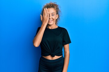 Poster - Beautiful caucasian teenager girl wearing black sportswear covering one eye with hand, confident smile on face and surprise emotion.