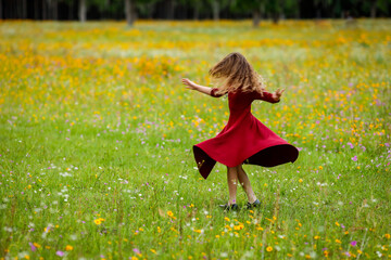 a little girl in a flower spins and dances in a red dress with motion blur