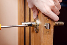 Door Installation, Worker Installs Door Knob, Woodworker Hands Close Up. A Man Spins The Door Handle With A Screwdriver, Repairs The Door Handle Mechanism