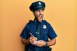 Handsome hispanic man wearing police uniform writing traffic fine angry and mad screaming frustrated and furious, shouting with anger. rage and aggressive concept.