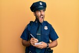 Fototapeta  - Handsome hispanic man wearing police uniform writing traffic fine angry and mad screaming frustrated and furious, shouting with anger. rage and aggressive concept.