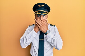 Canvas Print - Handsome hispanic man wearing airplane pilot uniform shocked covering mouth with hands for mistake. secret concept.