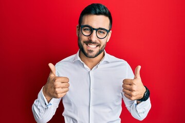 Young hispanic businessman wearing shirt and glasses success sign doing positive gesture with hand, thumbs up smiling and happy. cheerful expression and winner gesture.