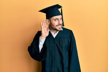 Wall Mural - Young hispanic man wearing graduation cap and ceremony robe smiling with hand over ear listening an hearing to rumor or gossip. deafness concept.
