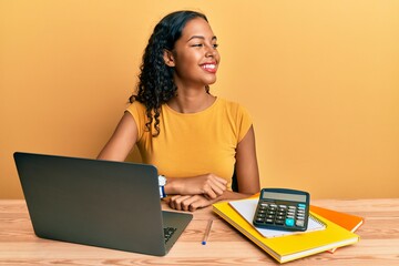 Poster - Young african american girl working at the office with laptop and calculator looking away to side with smile on face, natural expression. laughing confident.