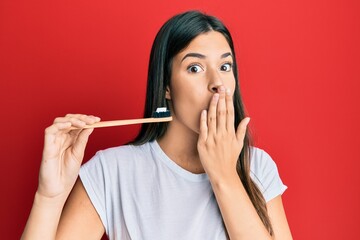 Sticker - Young brunette woman holding toothbrush with toothpaste covering mouth with hand, shocked and afraid for mistake. surprised expression