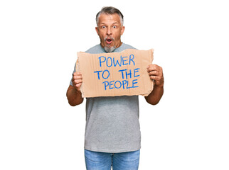 Canvas Print - Middle age grey-haired man holding power to the people banner scared and amazed with open mouth for surprise, disbelief face