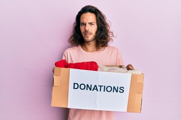 Poster - Young handsome man with long hair holding donations box for charity clueless and confused expression. doubt concept.