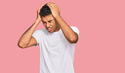 Poster - Young handsome african american man wearing casual white tshirt suffering from headache desperate and stressed because pain and migraine. hands on head.