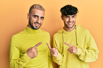 Sticker - Homosexual gay couple standing together wearing yellow clothes smiling and looking at the camera pointing with two hands and fingers to the side.