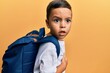 Adorable latin toddler worried wearing student backpack over isolated yellow background.