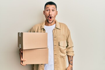 Poster - Handsome man with tattoos holding delivery package scared and amazed with open mouth for surprise, disbelief face