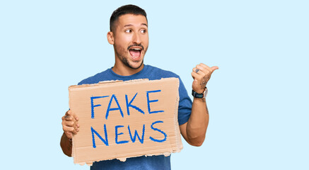 Poster - Handsome man with tattoos holding fake news banner pointing thumb up to the side smiling happy with open mouth