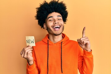 Young african american man with afro hair holding new word on paper smiling with an idea or question pointing finger with happy face, number one