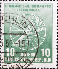 Wall Mural - GERMANY, DDR - CIRCA 1956  : a postage stamp from Germany, GDR showing a hand with a laurel branch in front of a spoked wheel. International Long Distance Cycling for Peace Warsaw-Berlin-Prague