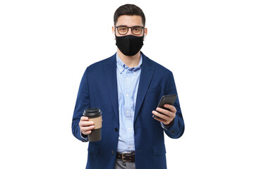 Wall Mural - Young business man wearing medical mask, holding smartphone and coffee, looking at camera isolated on gray background