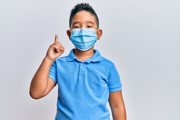 Canvas Print - Little boy hispanic kid wearing medical mask smiling with an idea or question pointing finger up with happy face, number one