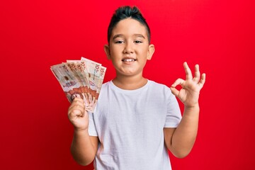 Poster - Little boy hispanic kid holding 10 colombian pesos banknotes doing ok sign with fingers, smiling friendly gesturing excellent symbol