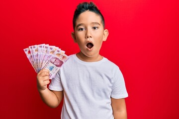 Canvas Print - Little boy hispanic kid holding 50 mexican pesos banknotes scared and amazed with open mouth for surprise, disbelief face