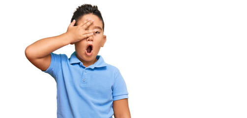 Sticker - Little boy hispanic kid wearing casual clothes peeking in shock covering face and eyes with hand, looking through fingers with embarrassed expression.