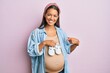 © Krakenimages.com - Beautiful hispanic woman expecting a baby holding shoes smiling happy pointing with hand and finger