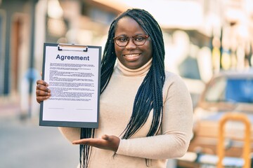 Young african american woman smiling happy holding clipboard with agreement contract at the city.