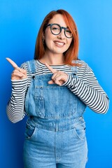 Wall Mural - Beautiful redhead woman wearing casual clothes and glasses smiling and looking at the camera pointing with two hands and fingers to the side.