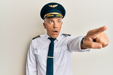 Wall Mural - Handsome middle age mature man wearing airplane pilot uniform pointing with finger surprised ahead, open mouth amazed expression, something on the front