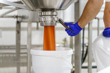 Close up on hand of unknown man wearing protective glove opening silos with cream or marmalade product at factory pouring in the bucket package - food factory concept