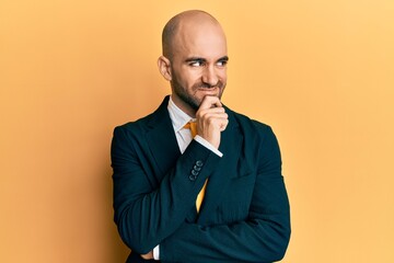 Wall Mural - Young hispanic man wearing business suit and tie with hand on chin thinking about question, pensive expression. smiling with thoughtful face. doubt concept.