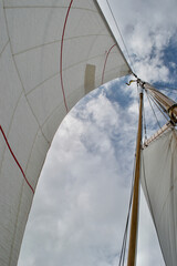  Looking up the mast of a gaff rigged sailing yacht: white sails, wooden mast and gaff, rope shrouds, halyards and sheets, and blue cloudy sunny sky