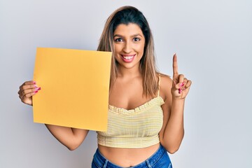 Poster - Beautiful brunette woman holding yellow blank empty banner smiling with an idea or question pointing finger with happy face, number one