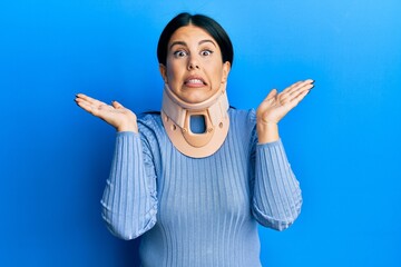 Poster - Beautiful brunette woman wearing cervical collar clueless and confused expression with arms and hands raised. doubt concept.