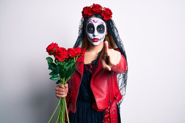 Sticker - Woman wearing day of the dead costume holding roses pointing with finger to the camera and to you, confident gesture looking serious