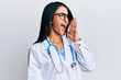 © Krakenimages.com - Beautiful hispanic woman wearing doctor uniform and stethoscope shouting and screaming loud to side with hand on mouth. communication concept.