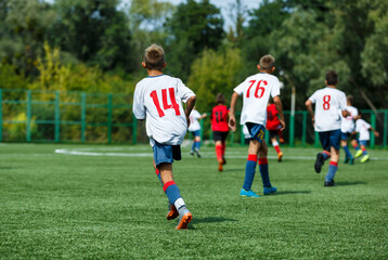 Wall Mural - Young sport boys in white sportswear running and kicking a  ball on pitch. Soccer youth team plays football in summer. Activities for kids, training	