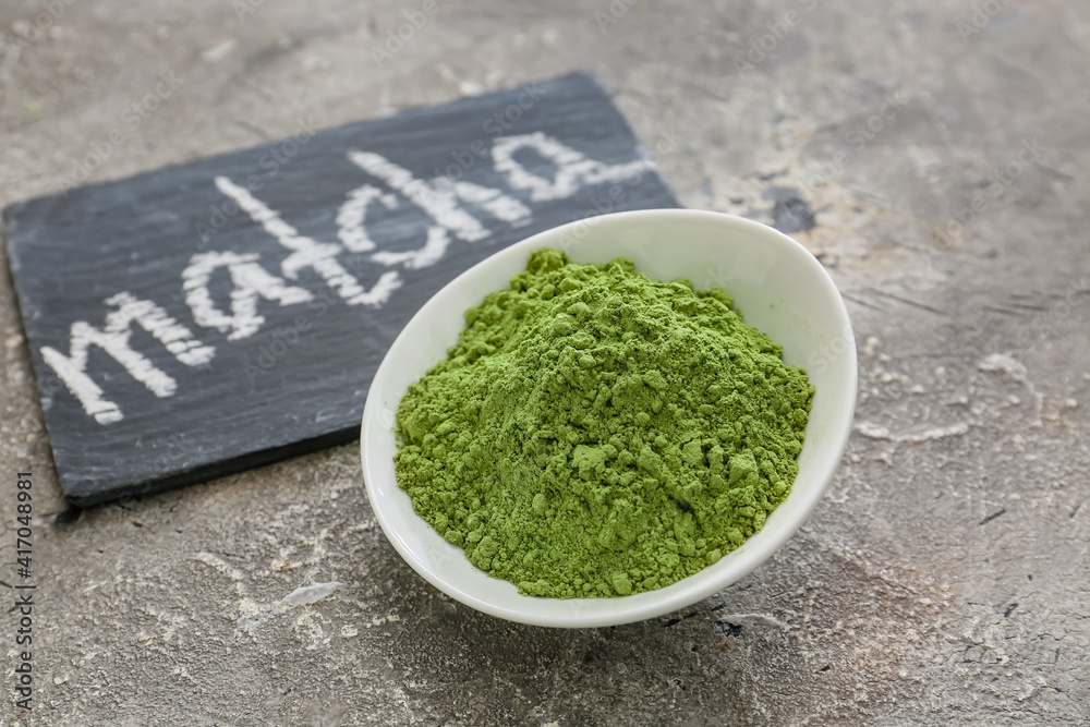 Slate board with word MATCHA and bowl with powder on dark background