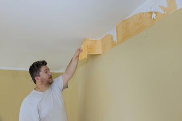 Man hand tear off old light wallpaper from wall preparing for home repair work removing wallpaper with a spatula