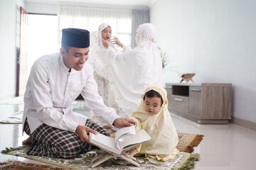 Wall Mural - portrait of happy muslim family with children reading quran and pray together at home