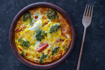 Frittata with egg, tomato, pepper, onion, broccoli and cheese on wooden table. Italian egg omelette