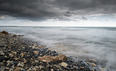 Wall Mural - Seawaves splashing to the coast with stones against stormy dramatic cloudy sky. Wintertime, Limassol cyprus