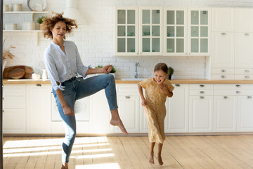 Wall Mural - Hilarious home party. Emotional family young single mother and small daughter having fun dance listen to music at new modern kitchen. Overjoyed nanny little kid girl jump barefoot on warm wooden floor